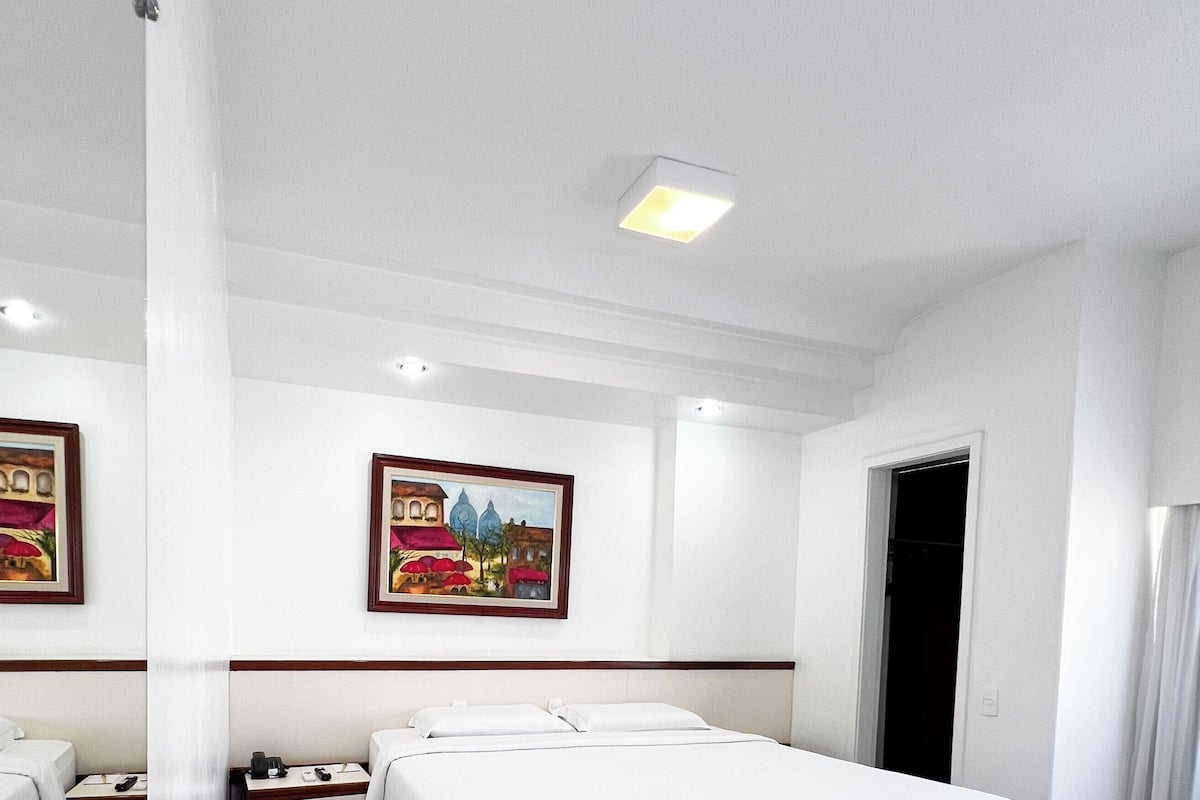 Ein Hotelzimmer mit einem großen Bett, zwei Nachttischen, einem Wandbild und einer Tür.