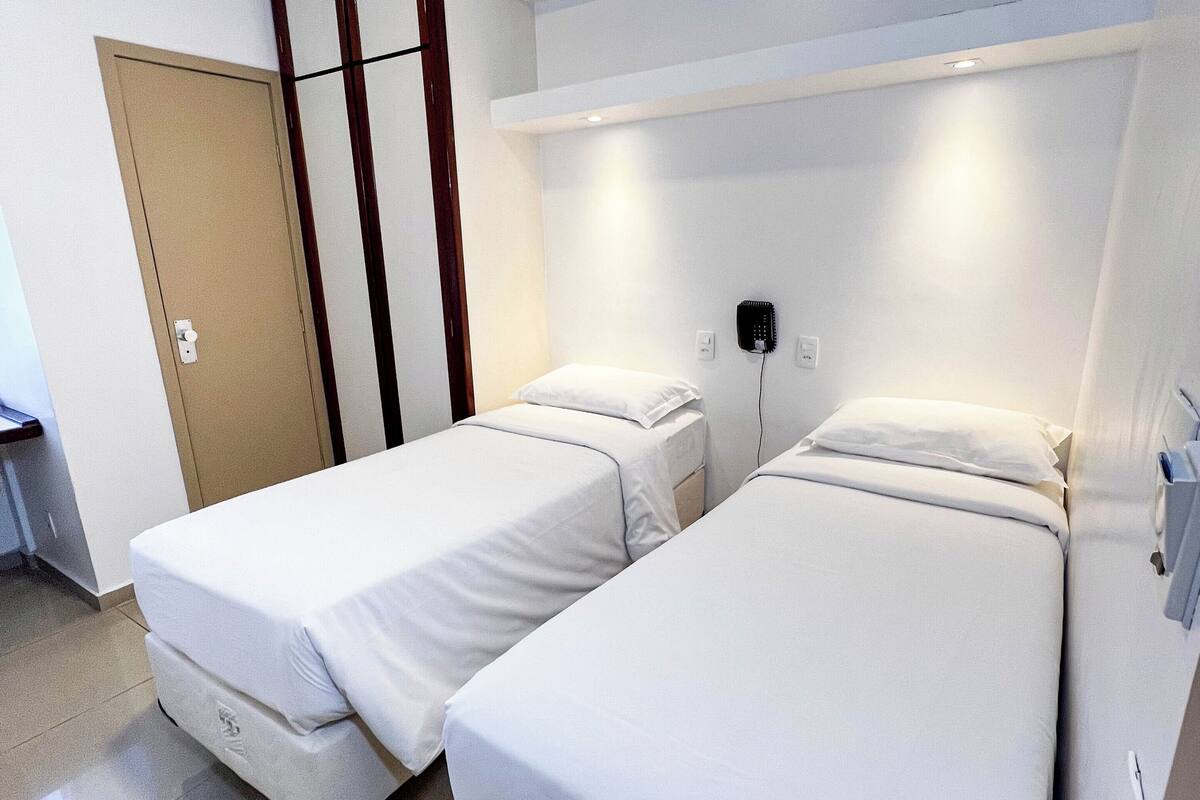 Ein Hotelzimmer mit zwei Einzelbetten, einer Tür, einem an der Wand montierten Fön und einem Lichtschalter.