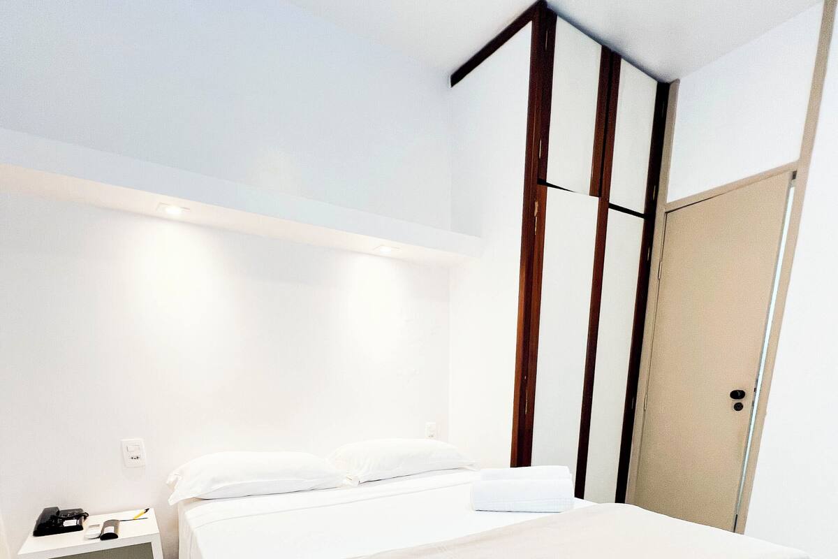 Ein modernes Hotelzimmer mit einem großen Bett, einem Nachttisch, einem Kleiderschrank und einer Wandleuchte.