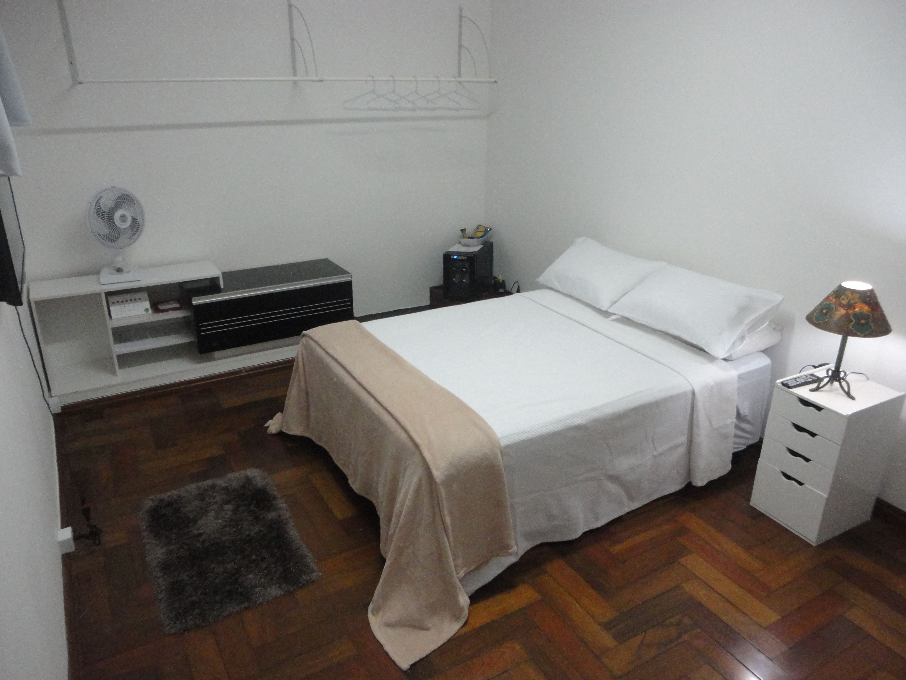 A bedroom with a bed, bedside table, lamp, and a small heater.