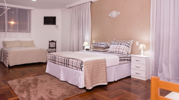 Un dormitorio con dos camas, suelo de madera, un ventanal grande y un televisor montado en la pared.