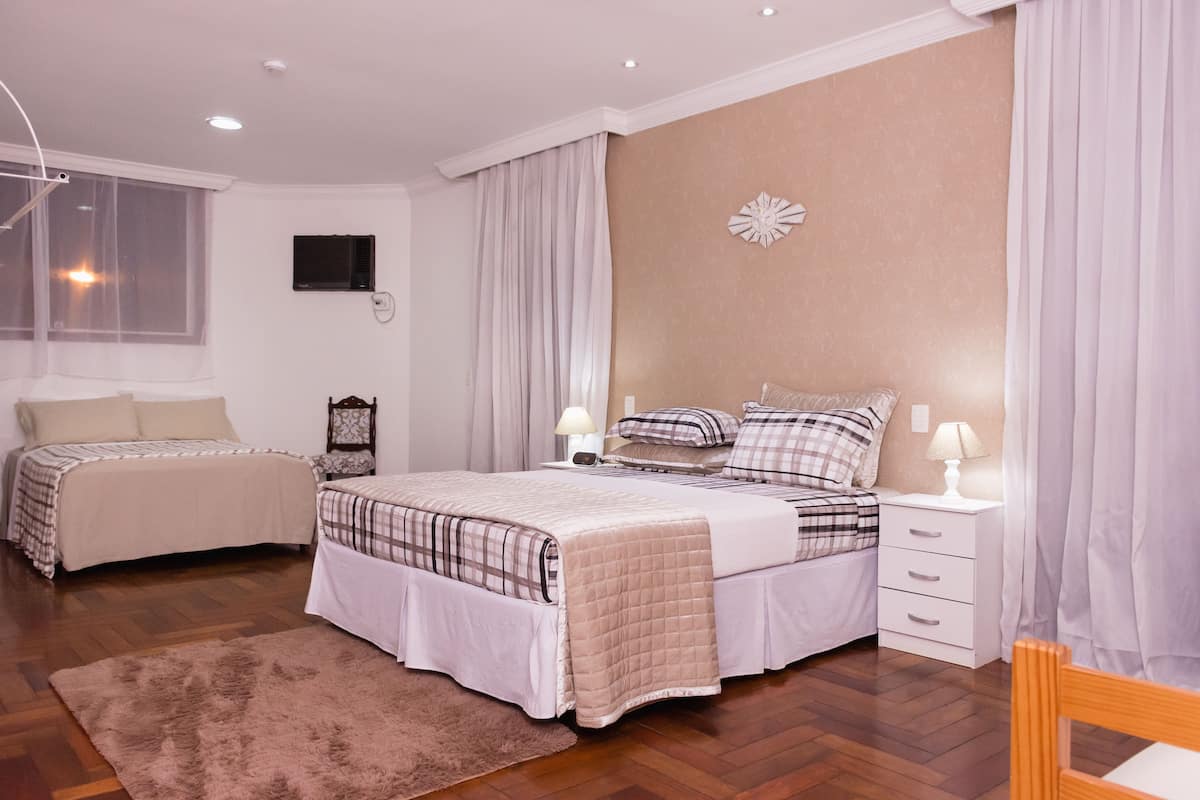 Un dormitorio con dos camas, suelo de madera, un ventanal grande y un televisor montado en la pared.
