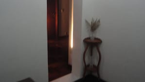 Un pasillo tenuemente iluminado, con una puerta de madera y una pequeña mesa con un florero.