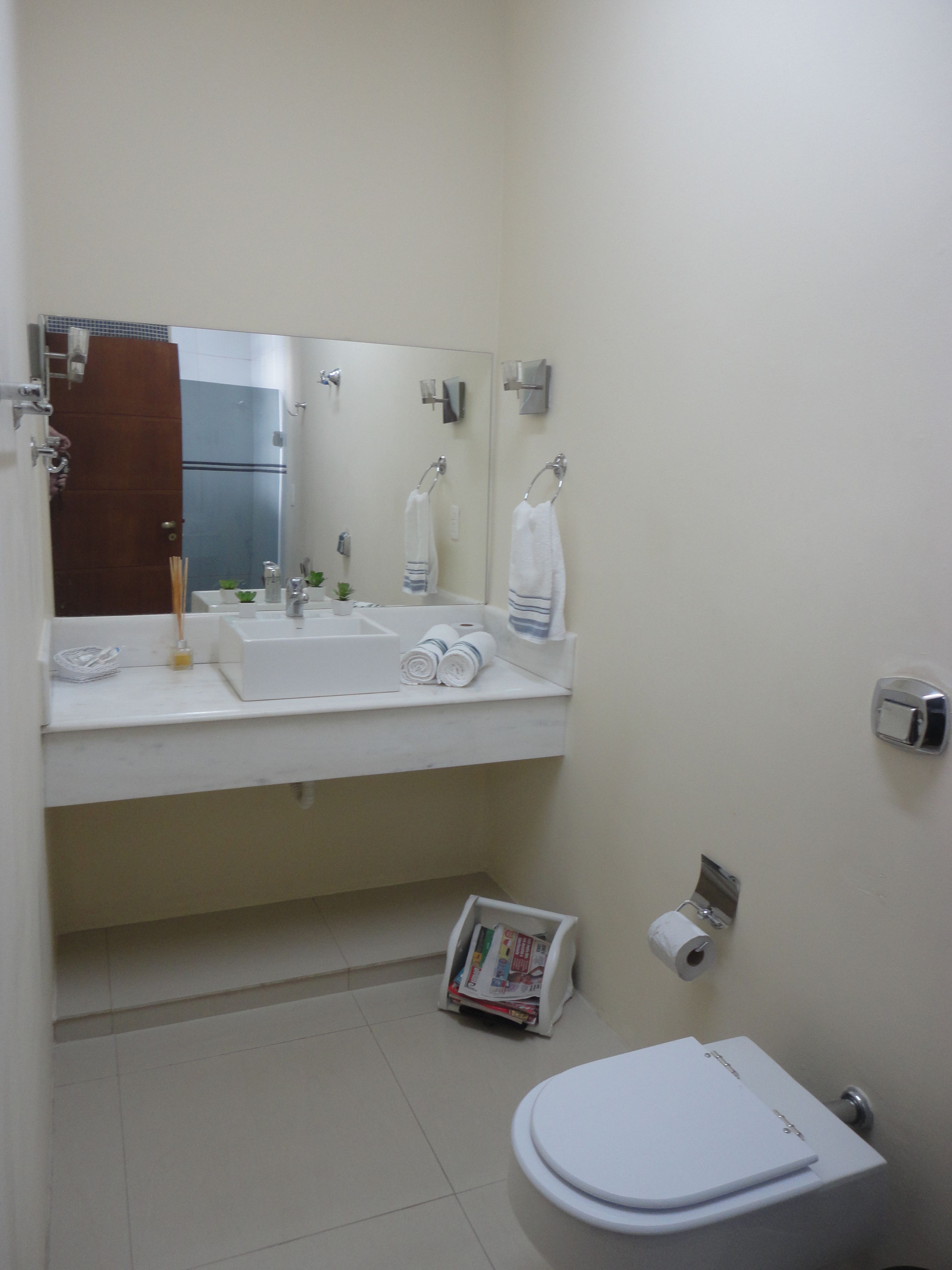 Une salle de bain avec un lavabo, un miroir et des toilettes blancs. On trouve des serviettes et des articles de toilette sur le comptoir du lavabo.