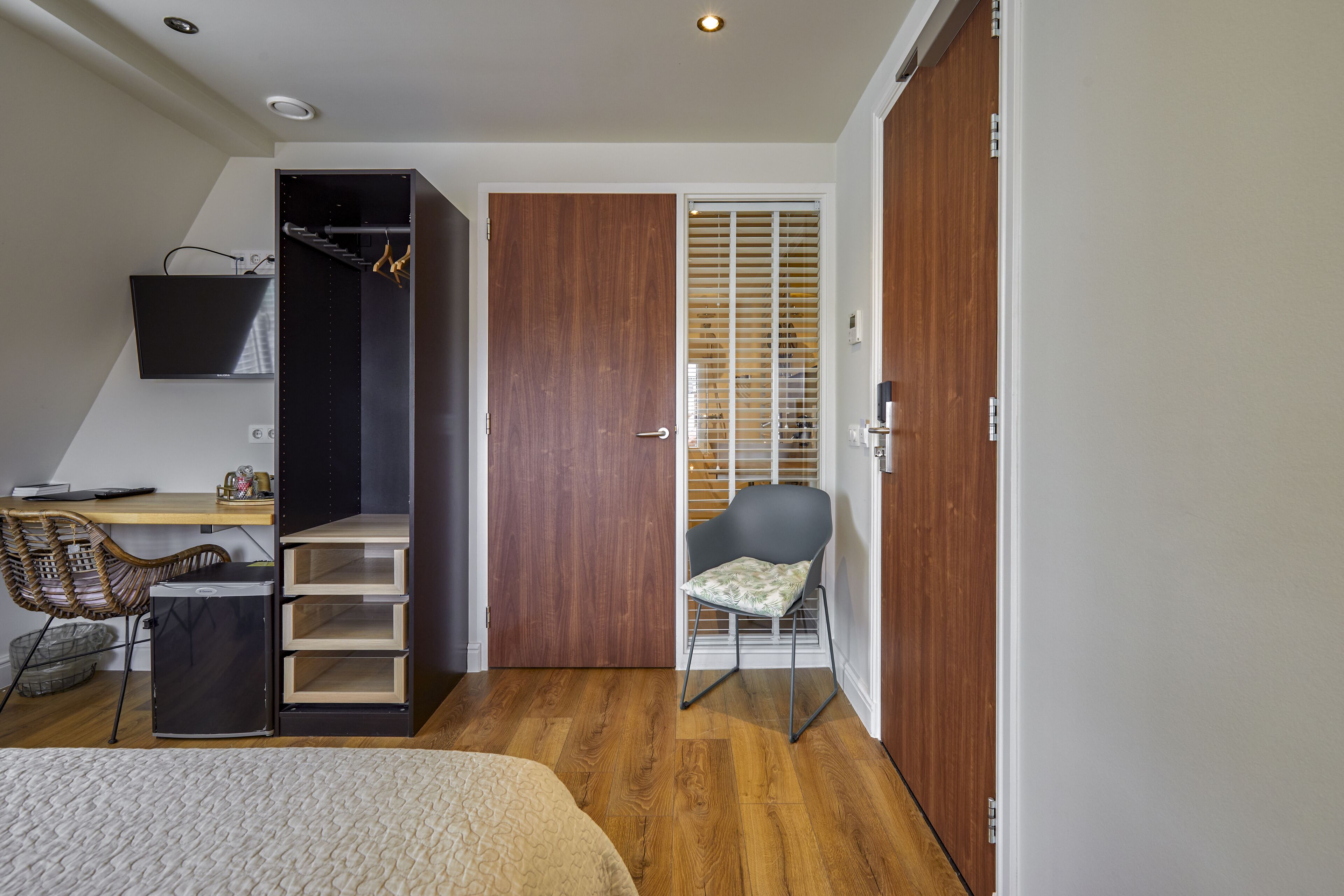 Ein Schlafzimmer mit einem Bett, einem Schreibtisch, einem Stuhl, einem Kleiderschrank und einer Schiebetür zum Balkon.