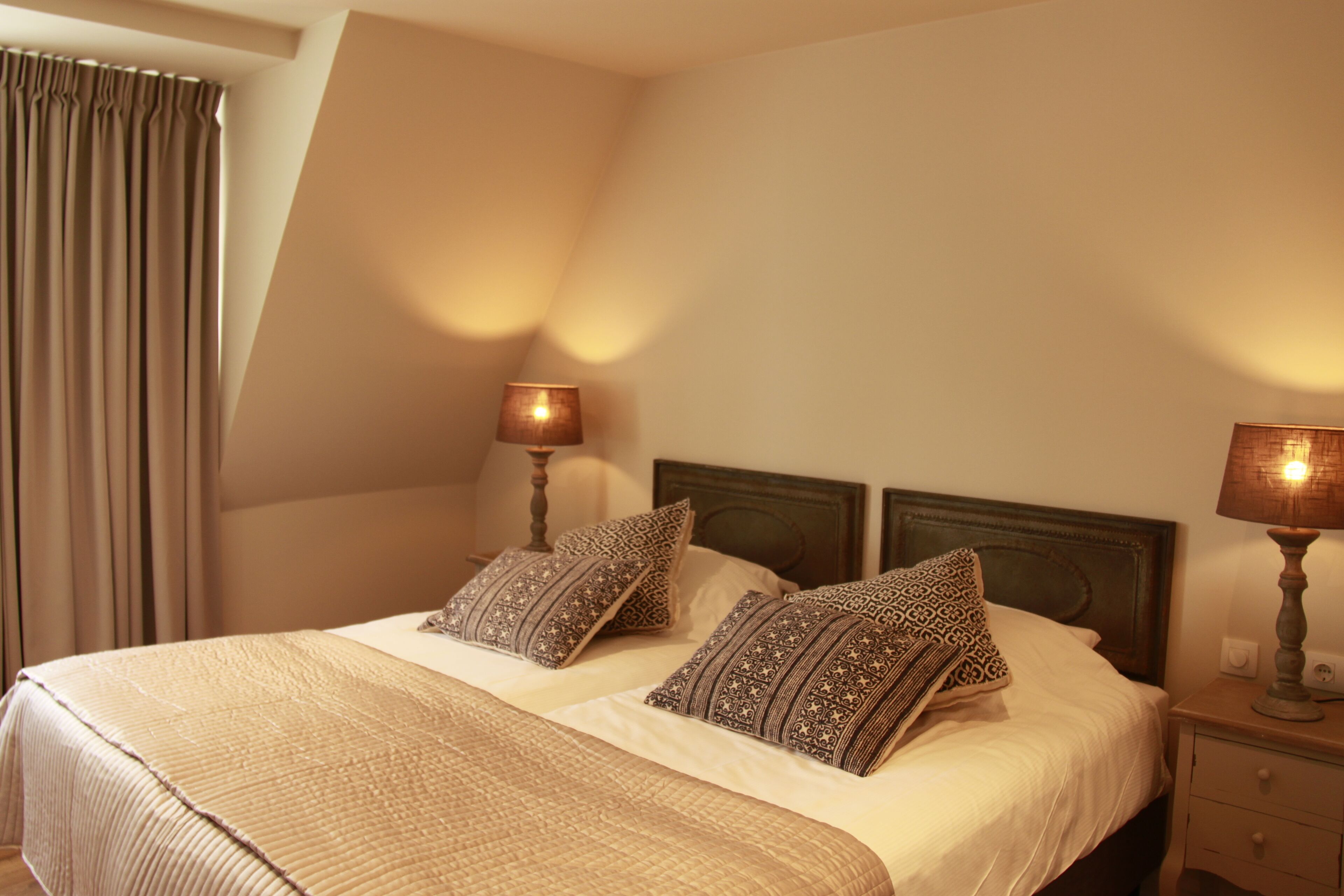 Une chambre d’hôtel avec un grand lit, deux tables de chevet et une fenêtre avec des rideaux.