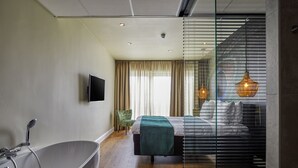 Une chambre moderne avec une grande baignoire, un lit recouvert d’une couverture verte et un téléviseur fixé au mur.