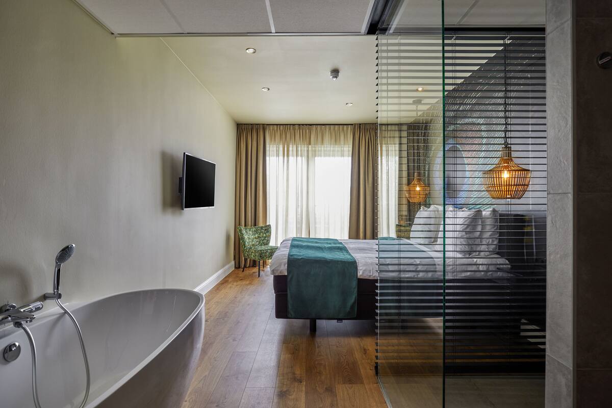 Een moderne slaapkamer met een groot bad, een bed met een groene deken en een tv aan de muur.