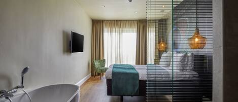 A modern bedroom with a large bathtub, a bed with a green blanket, and a TV mounted on the wall.