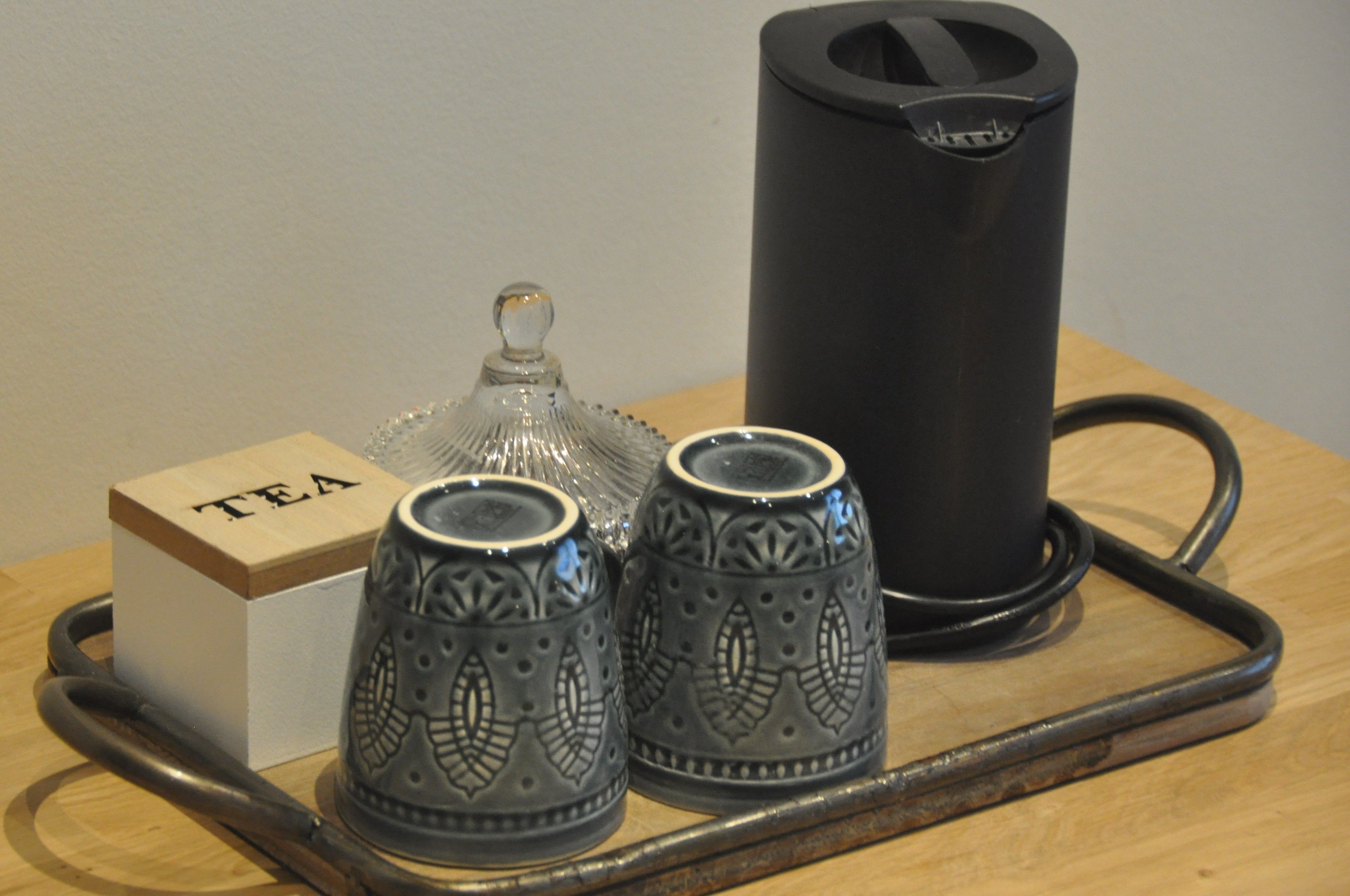 Un plateau avec une boîte à thé, deux tasses à motifs et une bouilloire noire.