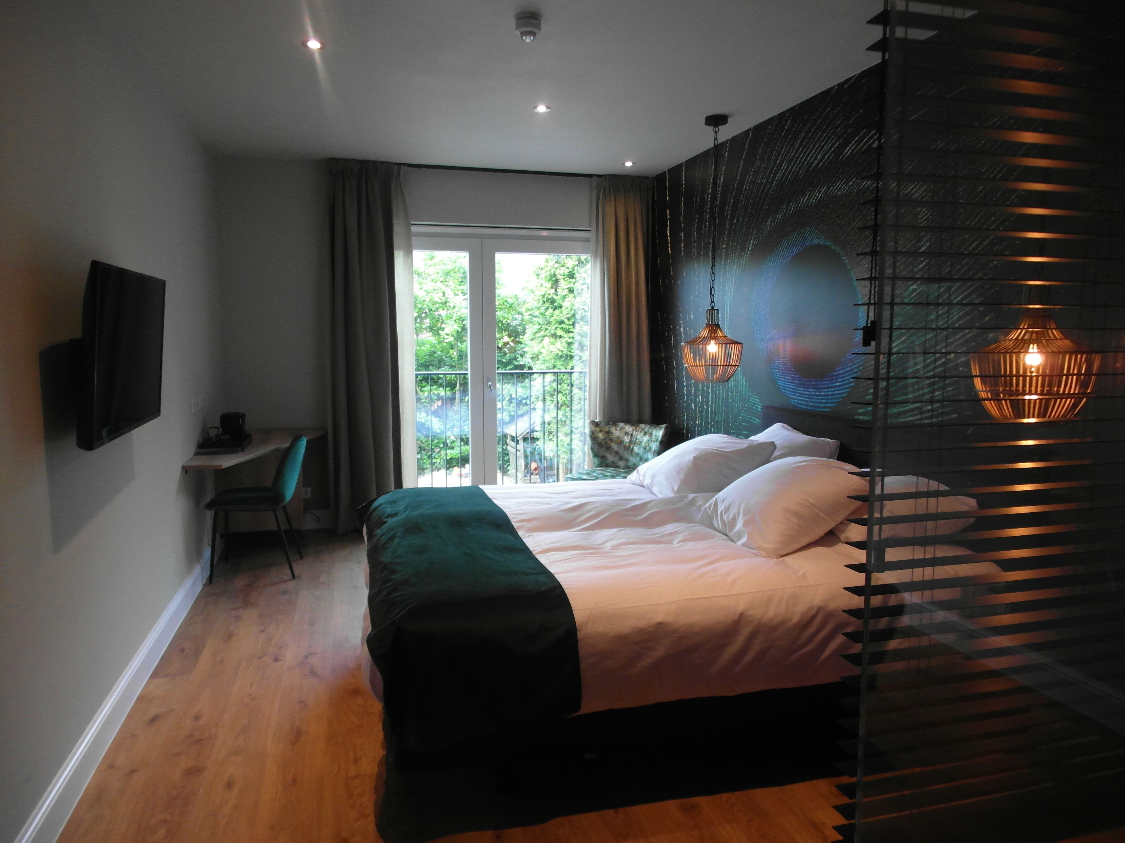Quarto moderno com uma cama grande, uma escrivaninha e vista para o verde lá fora.