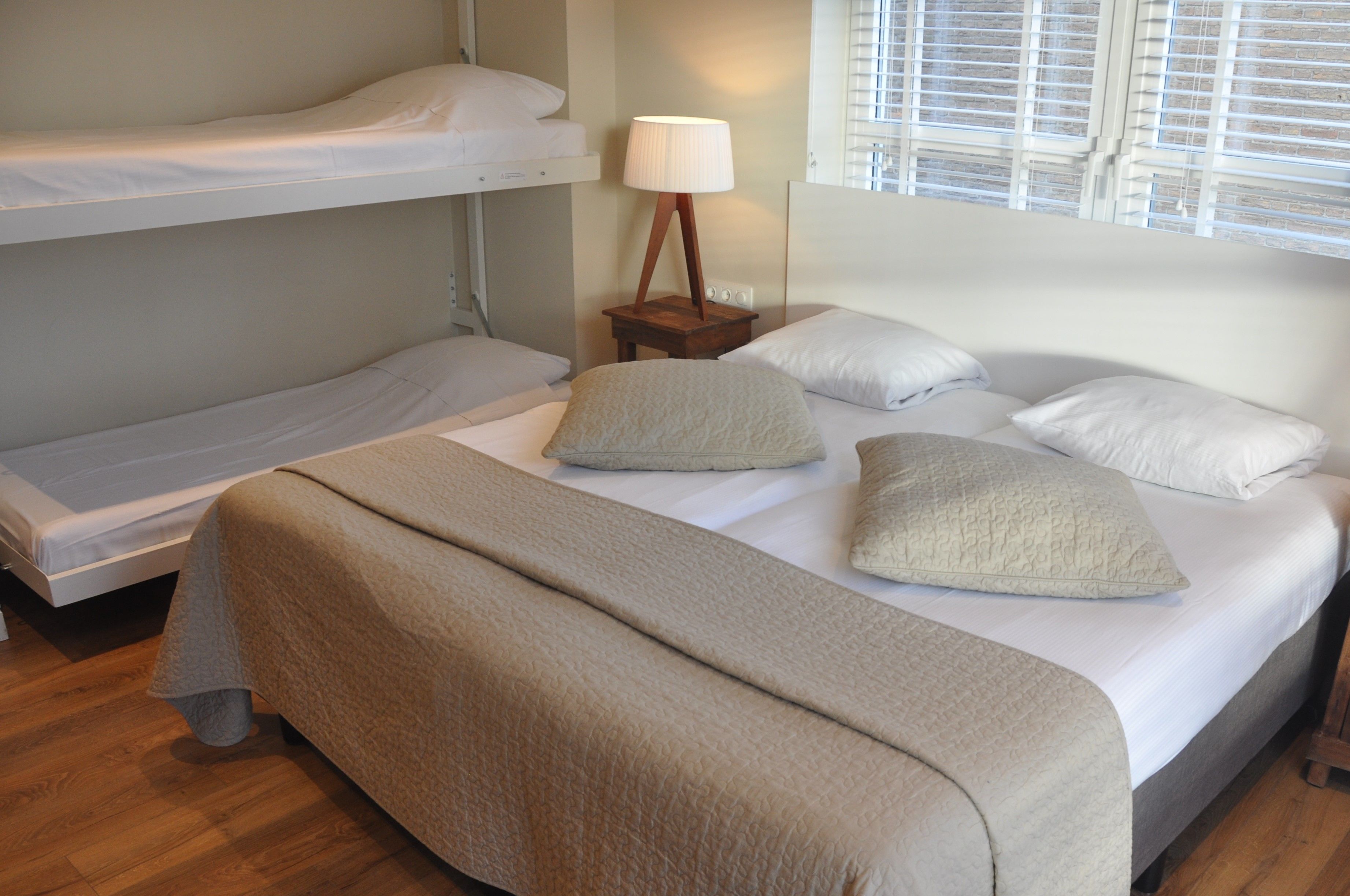 Een slaapkamer met een stapelbed, een enkel bed en een nachtkastje met een lamp.