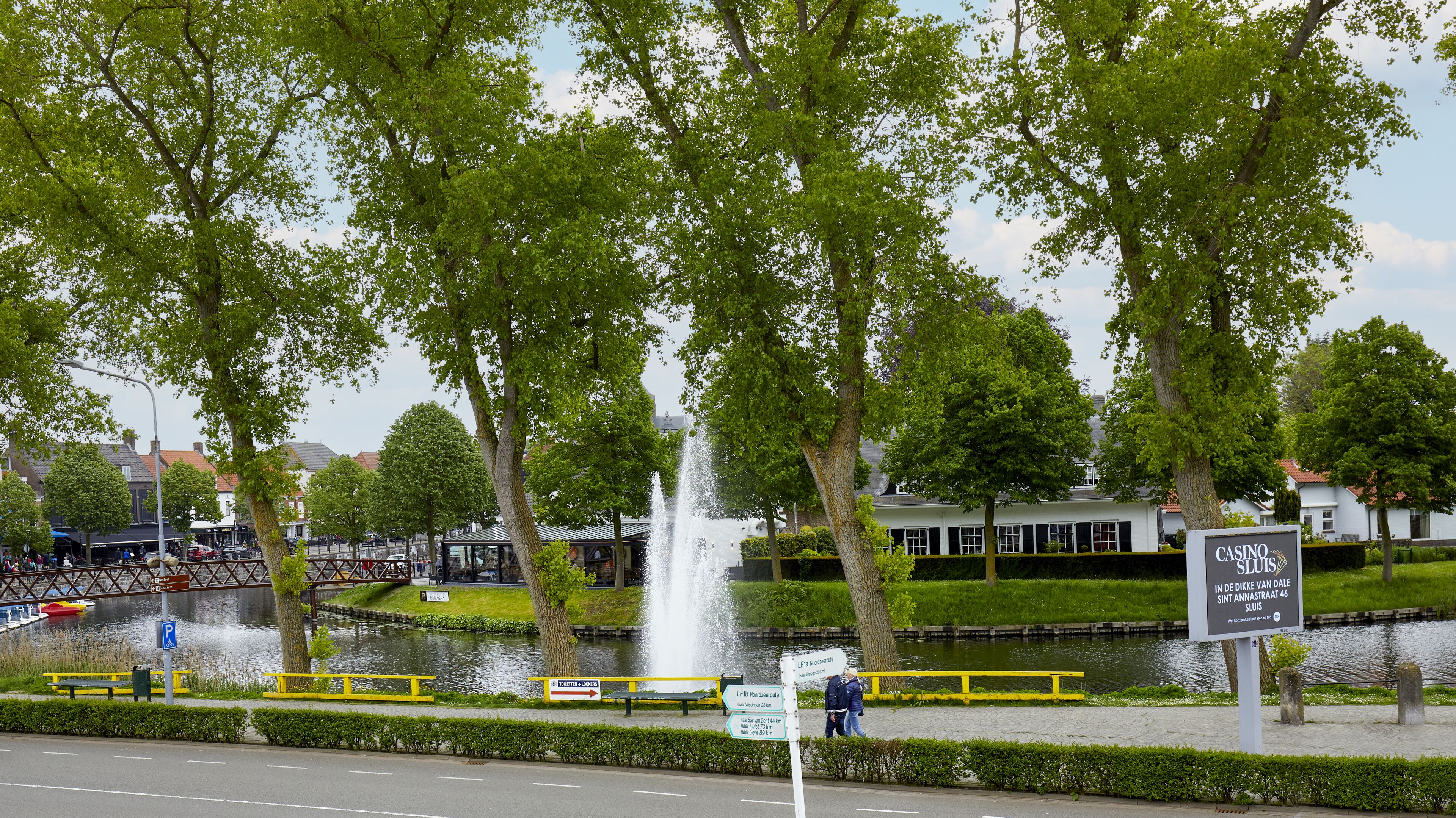 Un parque con una fuente, un cartel que dice 'Casino Sluis' y un canal con barcos.