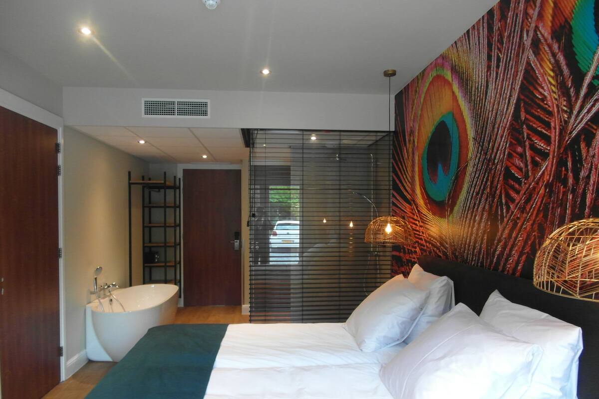Een slaapkamer met een groot bed, een badkuip en een muurschildering met pauwenveren.