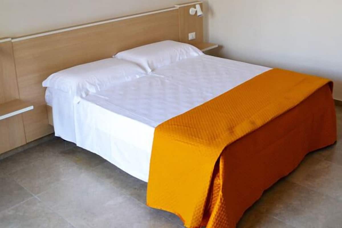 A single bed with white linens and an orange throw blanket.