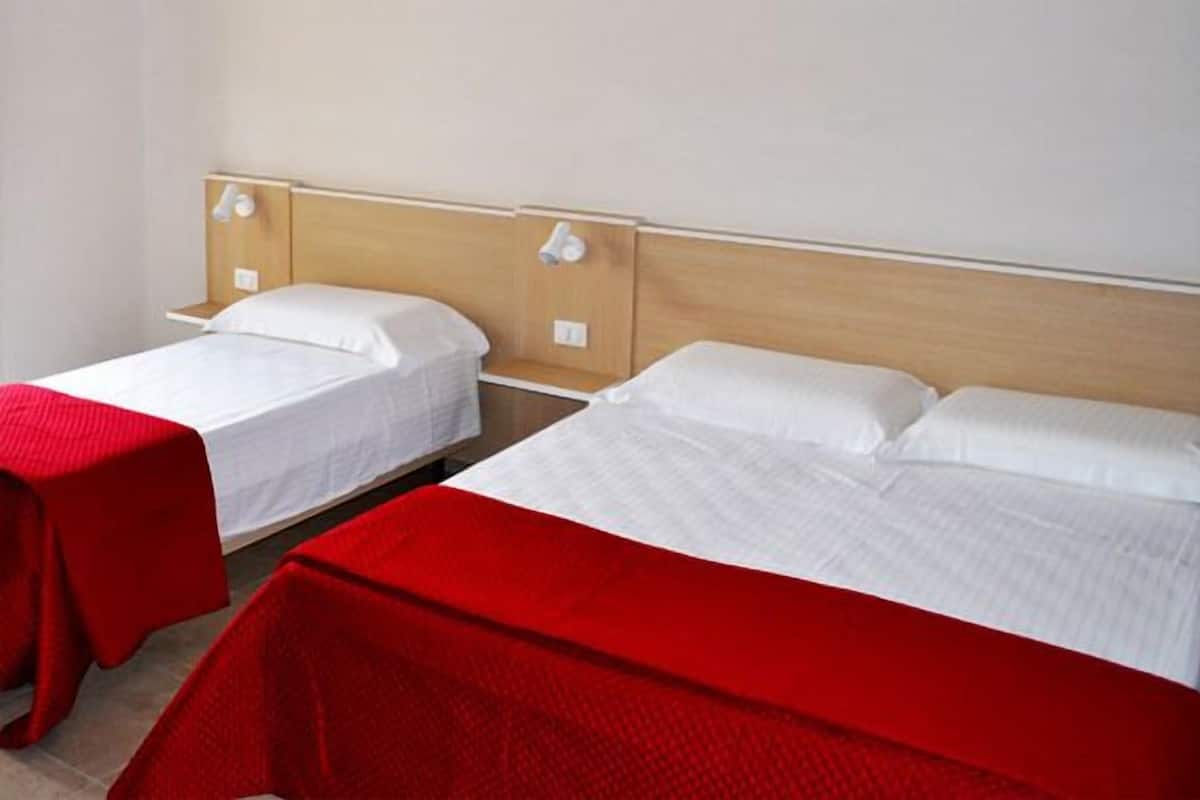 Two single beds with wooden headboards, white bedding, and red bedspreads in a room with plain walls and a tiled floor.