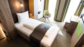 Ein Hotelzimmer mit einem Bett, einem Sessel, einem Schreibtisch und einer Wandlampe.