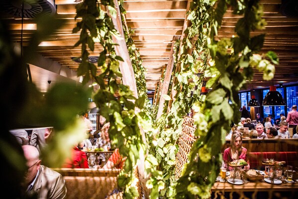 A restaurant with wooden ceiling beams, hanging plants, and patrons dining.