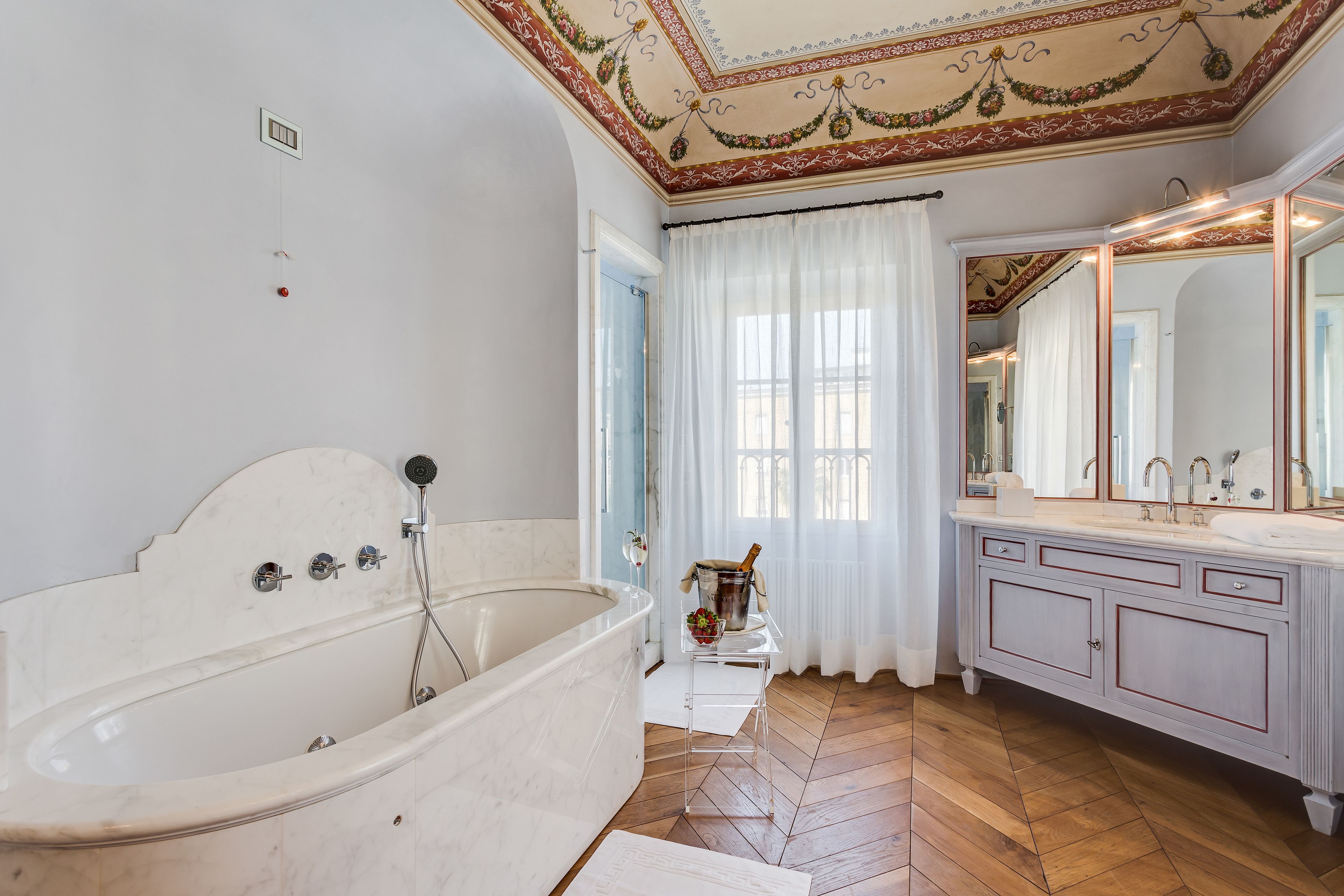 A spacious bathroom with a large bathtub, a vanity with a mirror, and a herringbone wood floor.