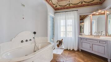 A spacious bathroom with a large bathtub, a vanity with a mirror, and a herringbone wood floor.