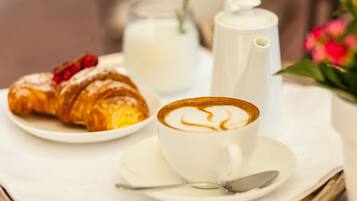 A breakfast setting with a croissant, a cup of coffee, a milk jug, and a teapot on a tray.