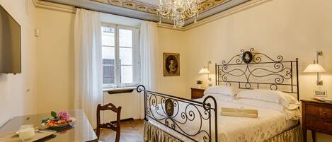 A bedroom with a bed, bedside lamps, a desk with a tray of breakfast, and a window with curtains.