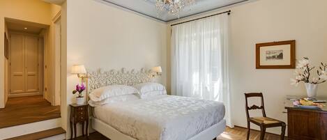 A bedroom with a large bed, a chandelier, a wooden floor, and a framed picture on the wall.