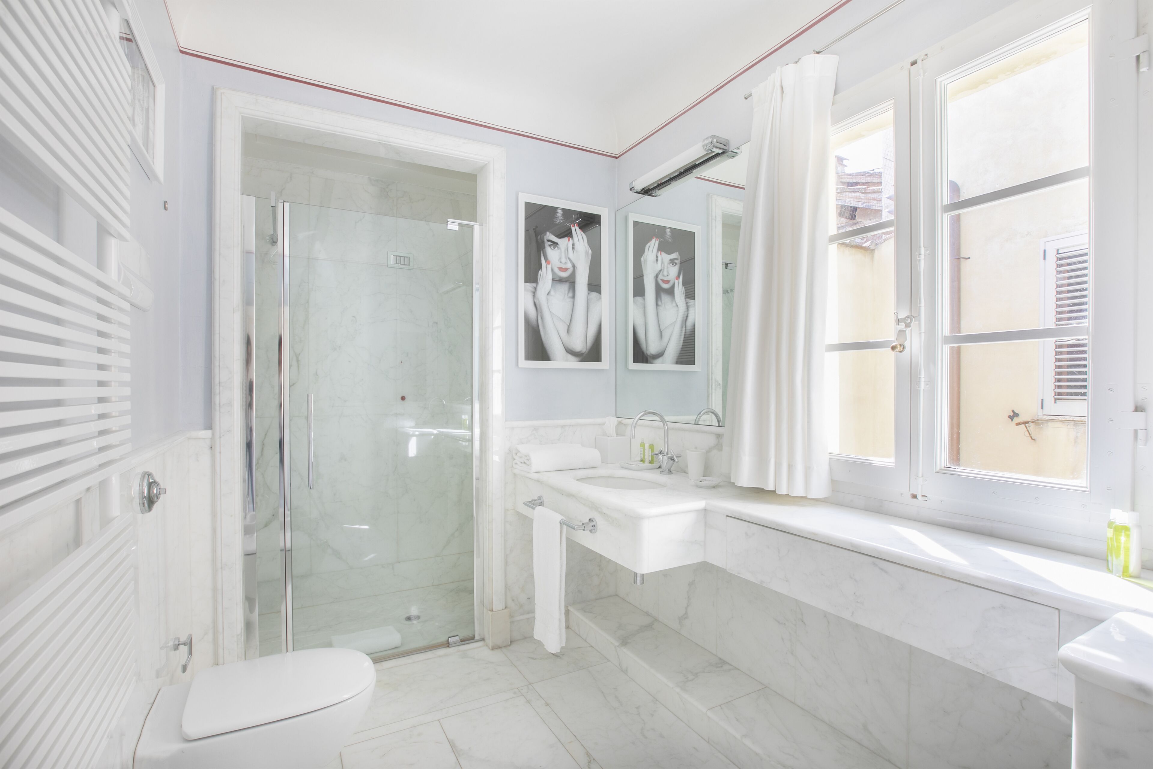 A modern bathroom with a glass shower enclosure, a white toilet, a sink with a mirror, and a window with curtains.