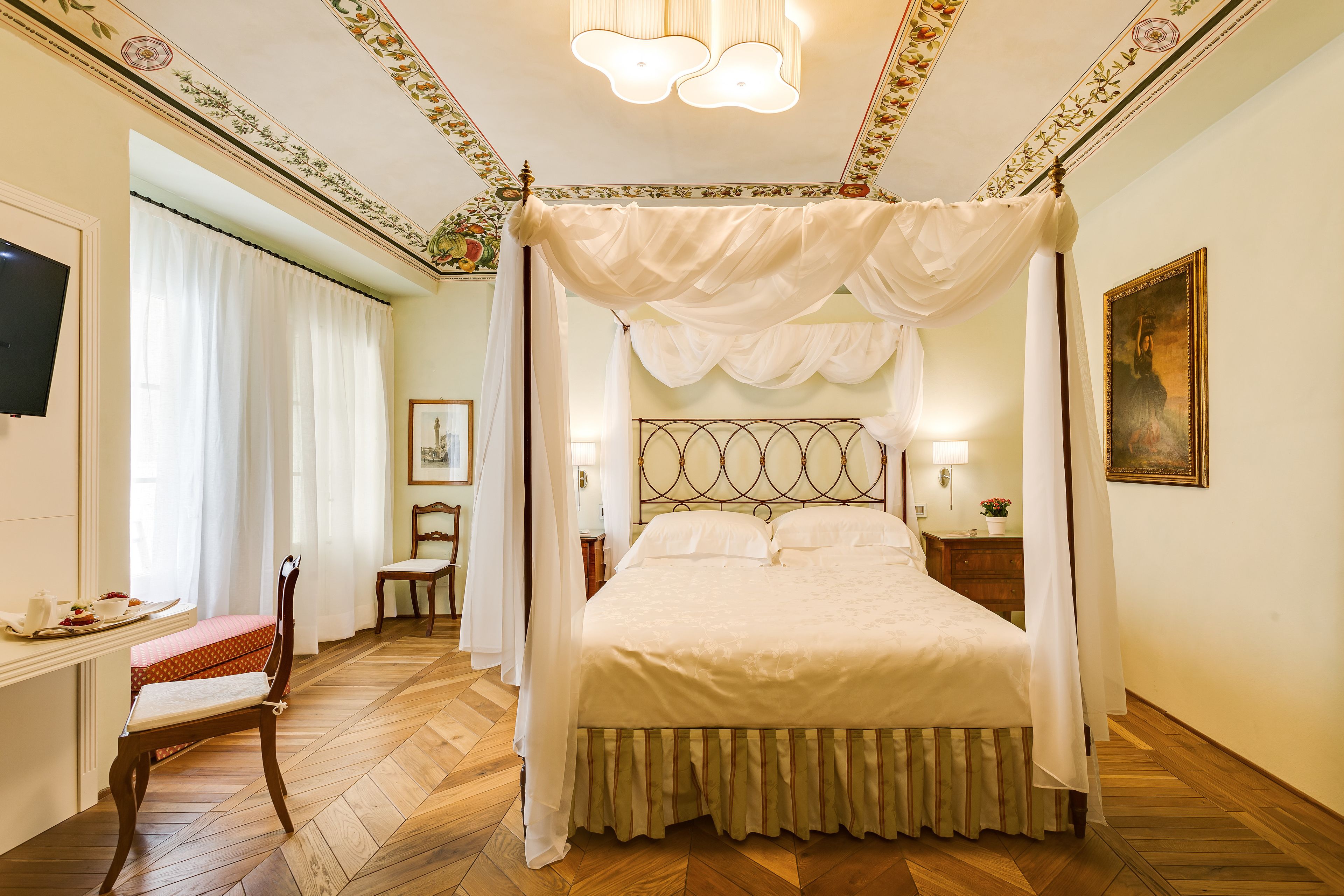 A four-poster canopy bed with a wooden headboard, a bedside table with a lamp, and a chair with a red cushion.