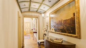 A hallway with a wooden floor, a painting on the wall, and a vase with flowers on a table. - Relais degli Angeli (Siena)