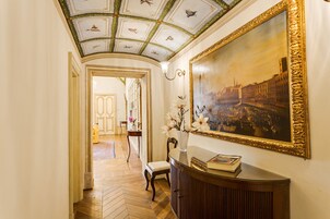 Un corridoio con pavimento in legno, un quadro appeso al muro e un vaso con fiori su un tavolo.