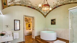 A bathroom with a large bathtub, wooden flooring, and a chandelier. - Relais degli Angeli (Siena)