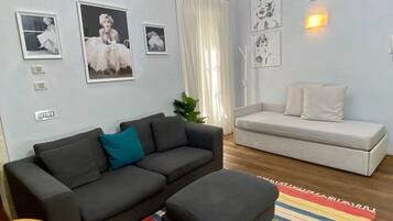 Una sala de estar con un sofá gris oscuro, un sofá blanco y un tapete de rayas de colores. Hay lámparas fijadas a la pared y cuadros enmarcados.