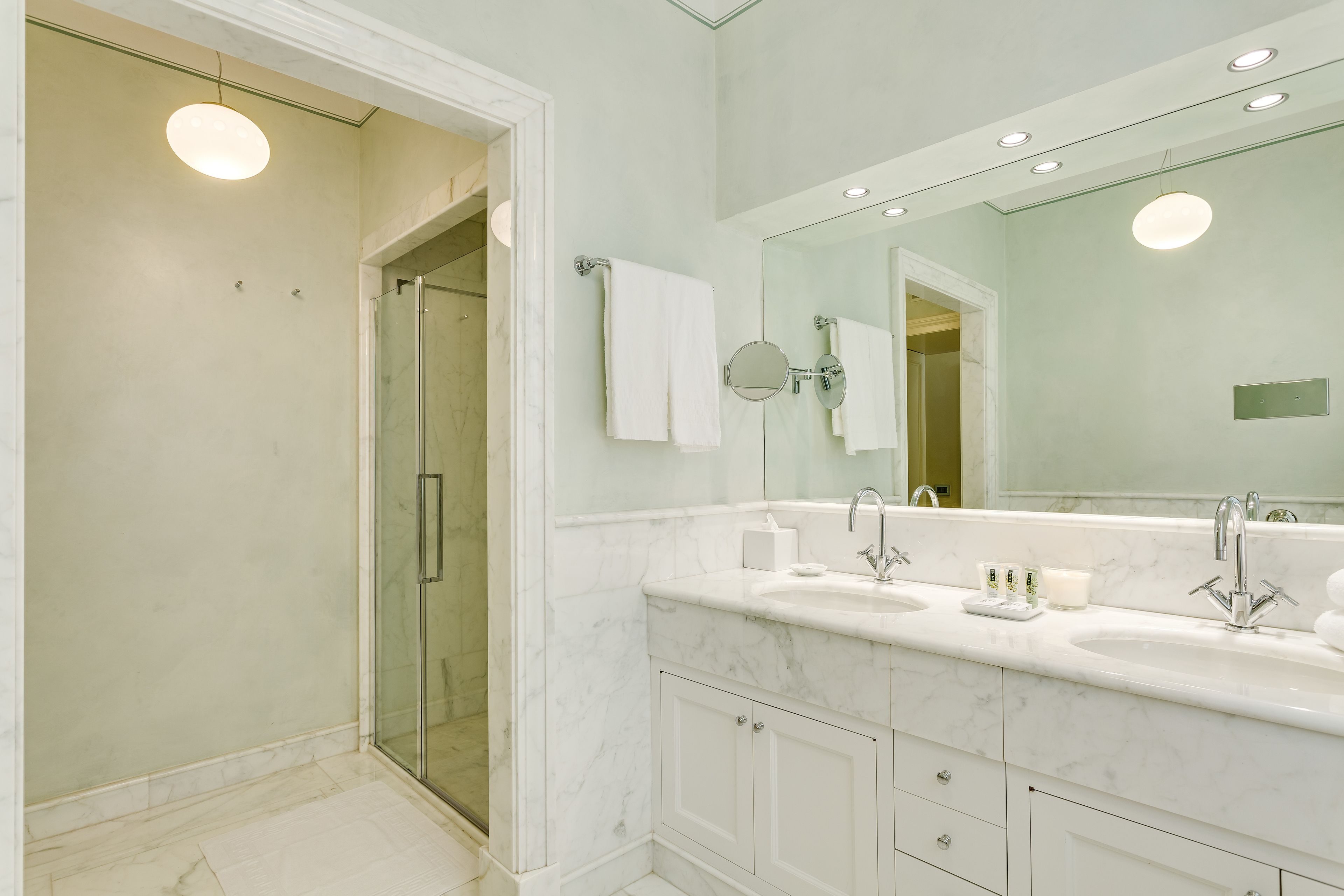 A bathroom with a glass-enclosed shower, a large mirror, and a double sink vanity.