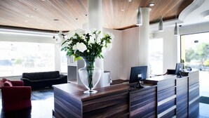 A reception desk with a vase of white flowers, a black sofa, and a red chair. - Brivali Hotel e Eventos (Cacador)