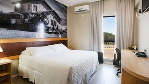 A hotel room with a bed, a desk with a lamp, a desk phone, and a wall-mounted air conditioner. - Brivali Hotel e Eventos (Cacador)