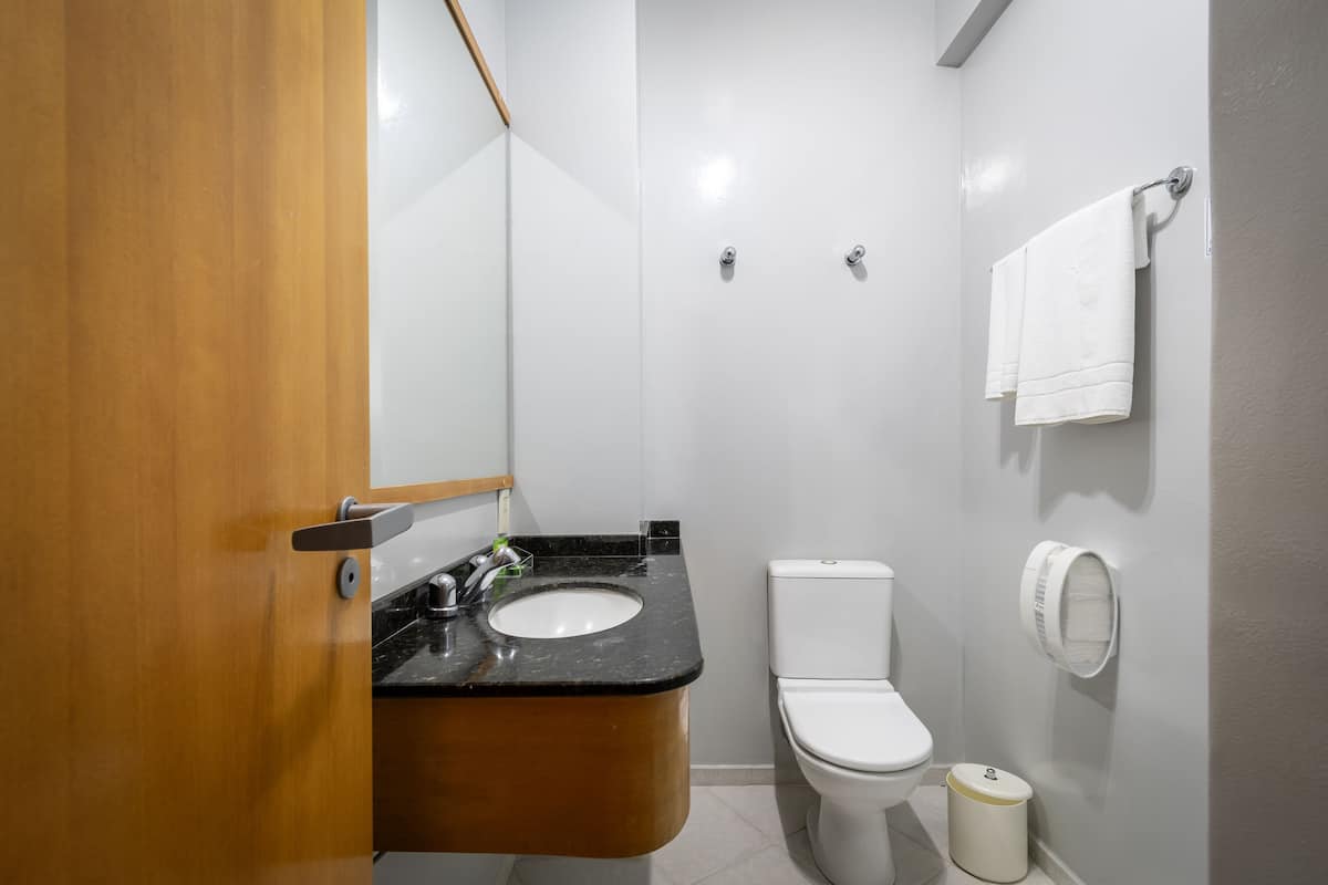 Un baño con puerta de madera, un lavabo negro, un inodoro blanco y un perchero para toallas.