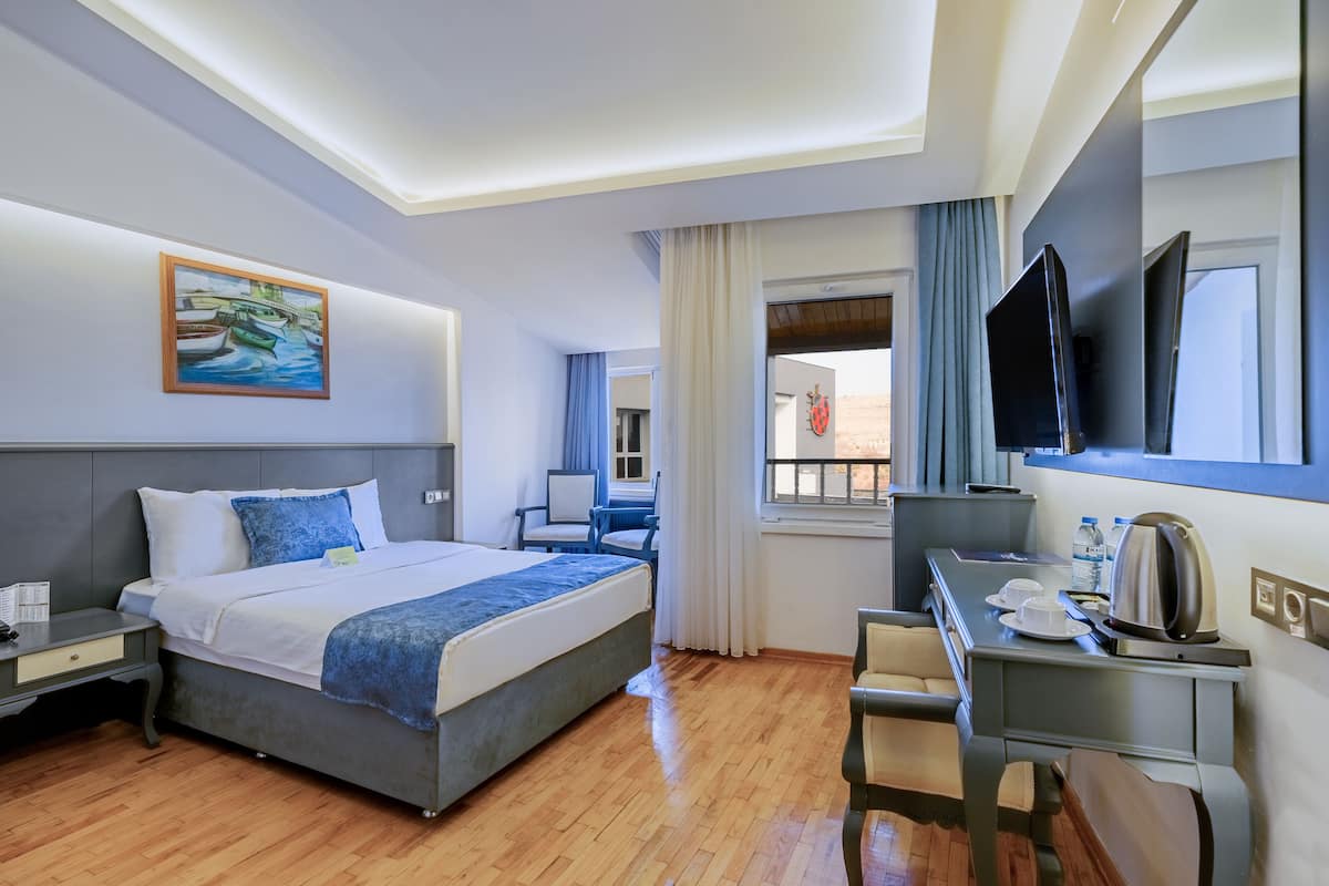 Habitación de hotel con cama, escritorio, silla, televisor y una obra de arte en la pared.