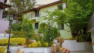 Un edificio con balcón, rodeado de vegetación y una estatua.