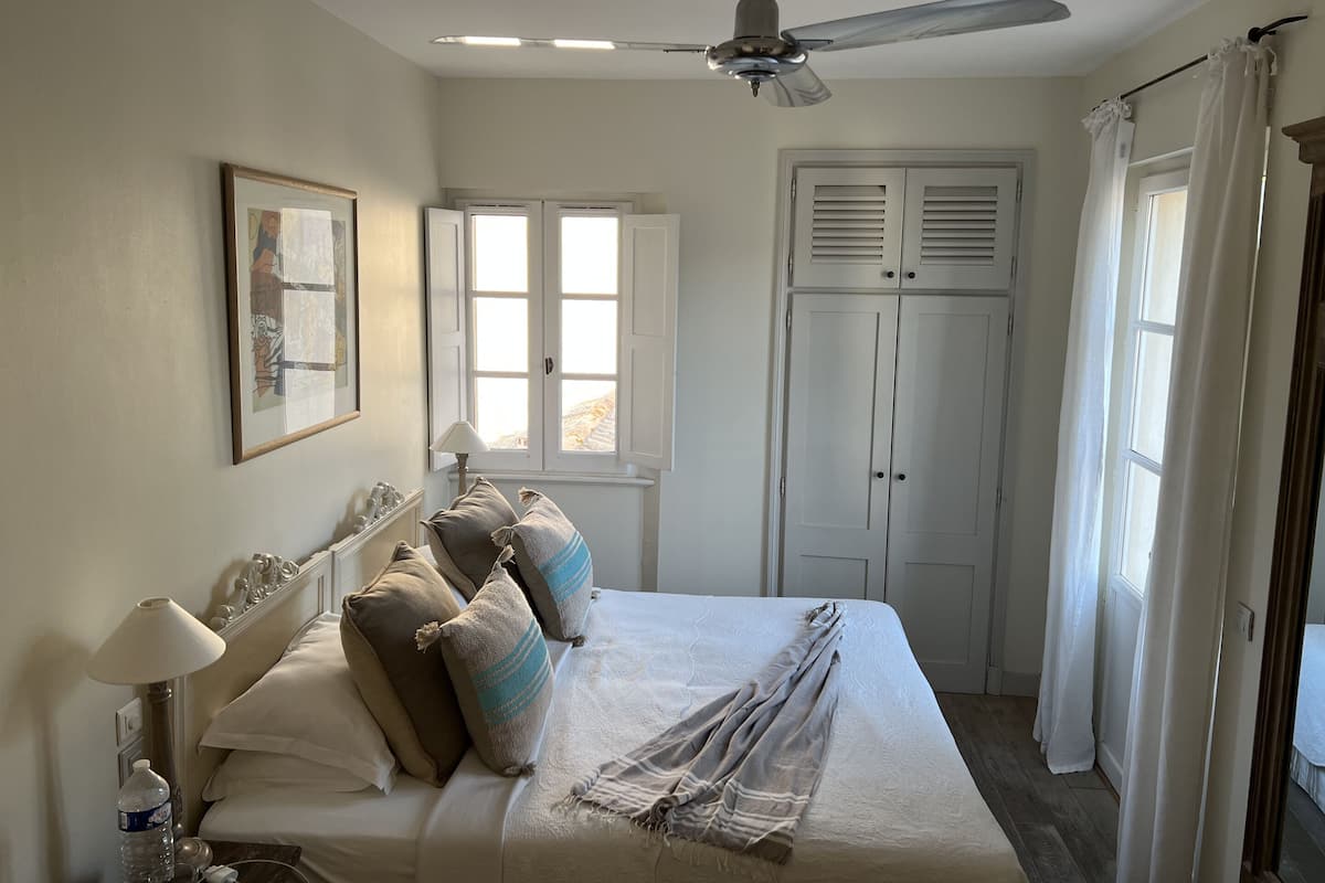 A bedroom with a bed, a ceiling fan, a window, and a door.