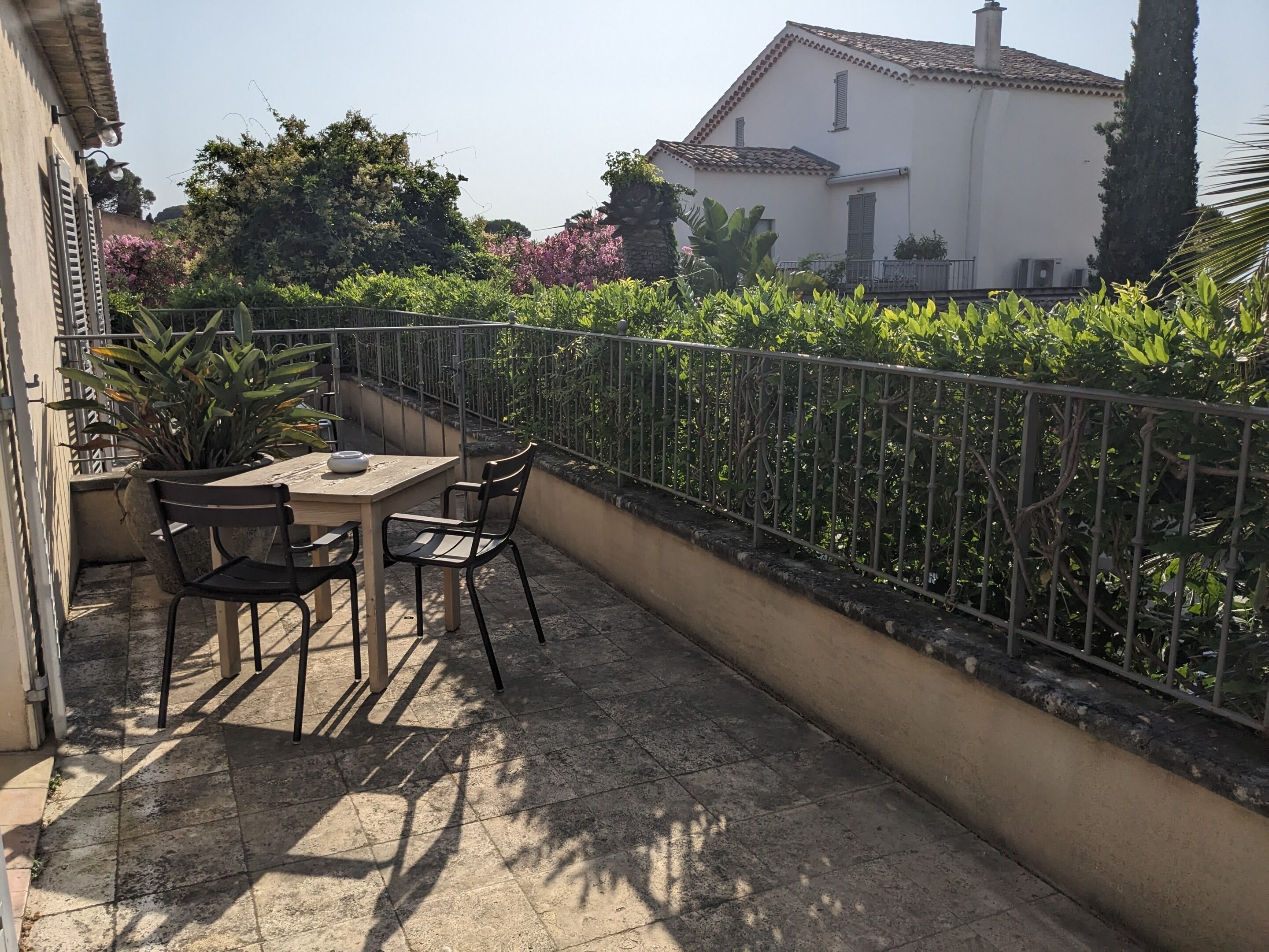 Un balcon agrémenté d’une table et de chaises, entouré d’une rambarde en métal et d’une végétation luxuriante.