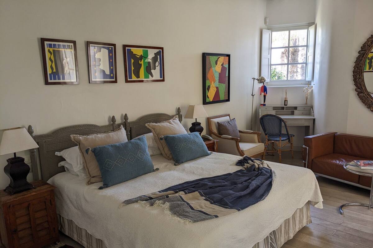 A bedroom with a large bed, a desk, a chair, and a window.