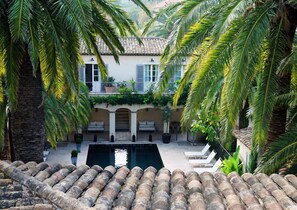 Un patio con piscina, palmeras y un edificio de techo con tejas y persianas.