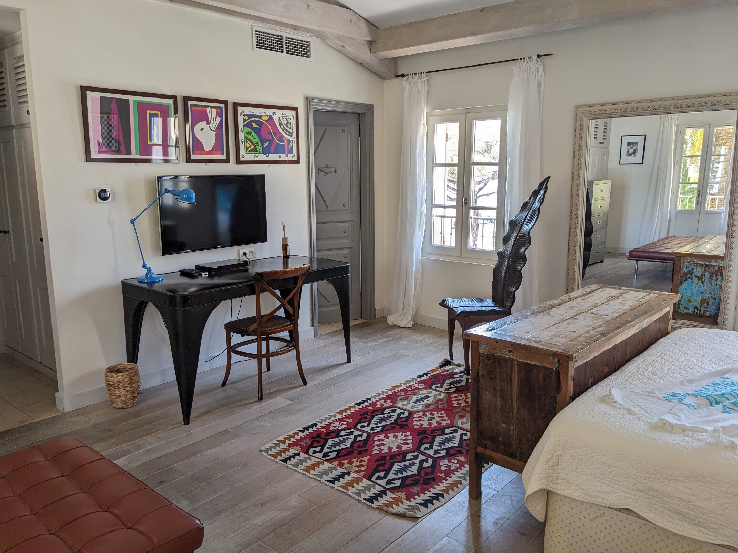A bedroom with a bed, a desk with a chair, a television, and a window with curtains.