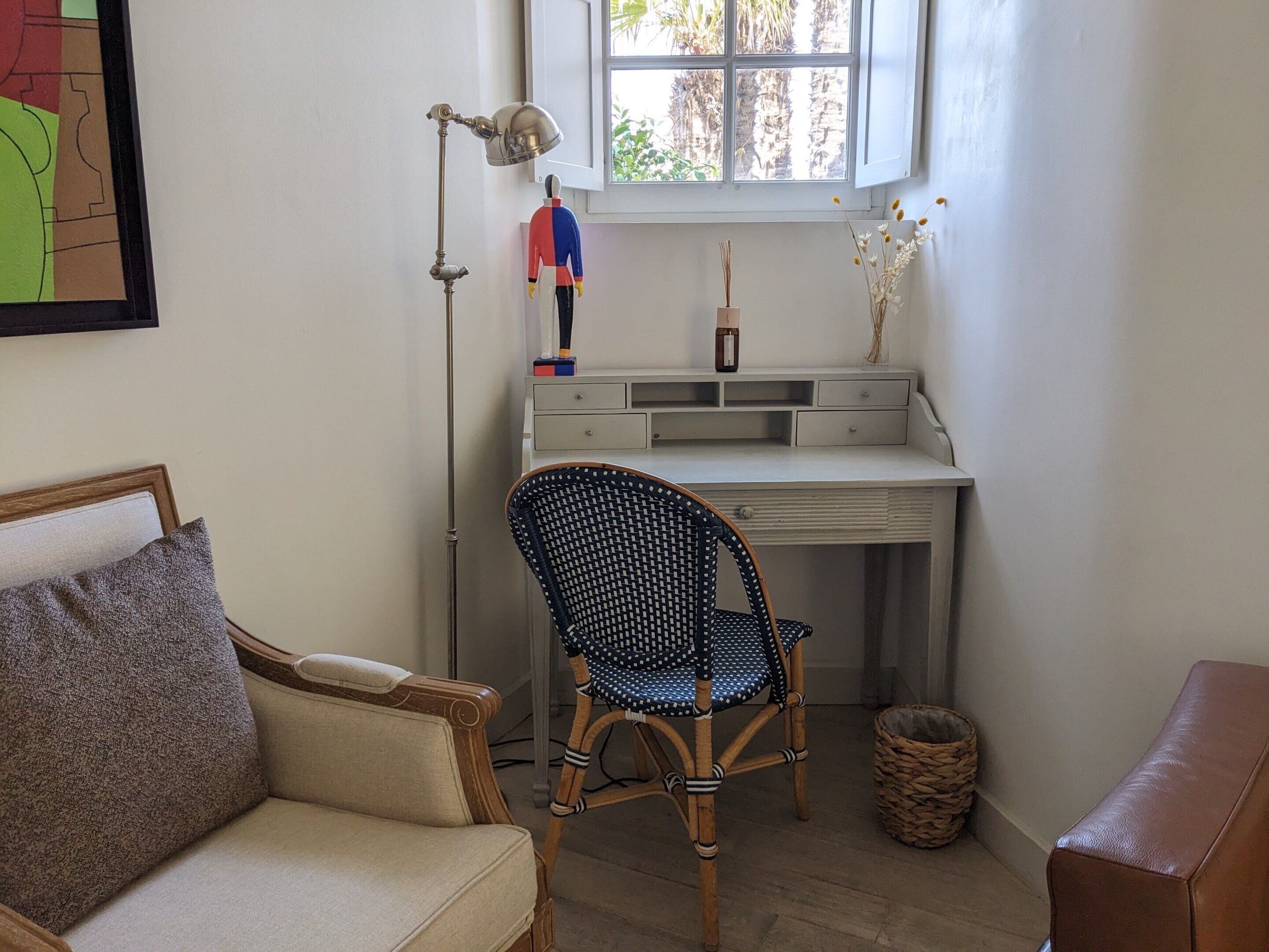 A cozy room with a desk, a wicker chair, a cushioned sofa, and a floor lamp.