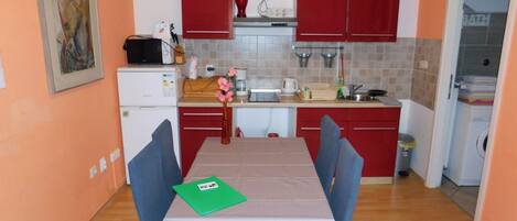 A compact kitchen with red cabinets, a white refrigerator, and a dining table with blue chairs.