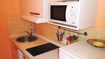 A compact kitchen with a sink, a microwave, and a stove. There are utensils hanging on a rack above the stove.