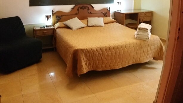 A bedroom with a bed, a desk, a chair, a nightstand, a ceiling fan, and a painting on the wall. - Walter Guest House (Rome)