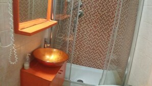 A bathroom with a glass shower enclosure, a white toilet, and a red vanity with a copper bowl sink. - Walter Guest House (Rome)