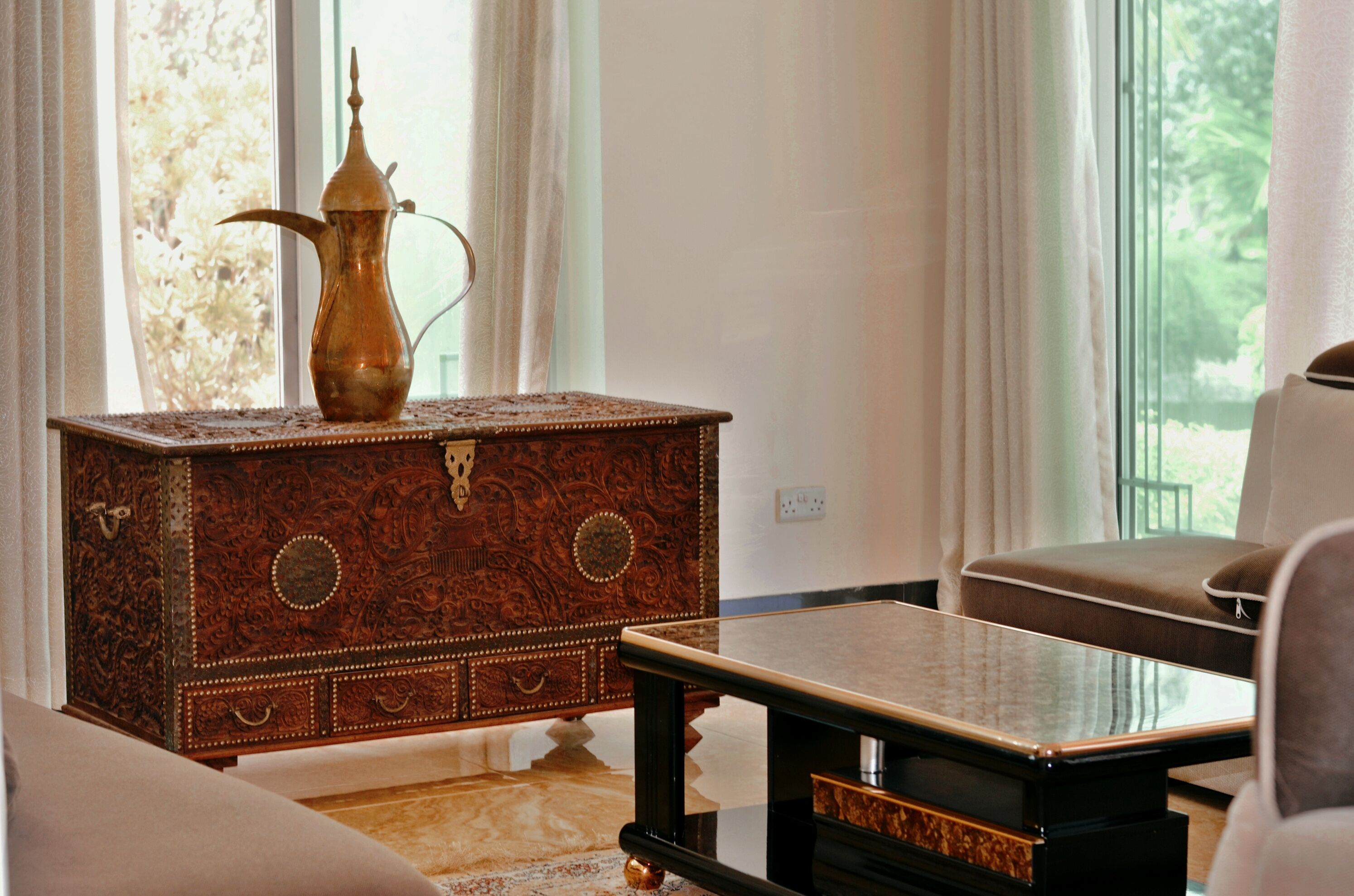 A room with a wooden chest of drawers, a glass-top table, and a cushioned chair.
